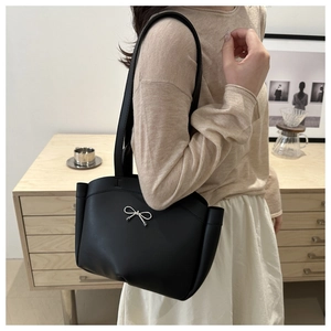 Detail of a black large-capacity tote bag with a silver metal bow on a model