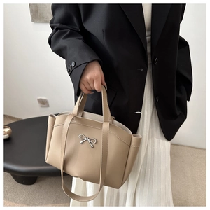Detail of beige tote bag with silver metal bow and textured synthetic leather finish