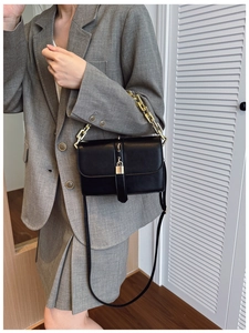 Sac chic en cuir noir avec poignée chaîne dorée et cadenas décoratif sur costume gris