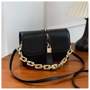 Détail d'un petit sac carré noir avec chaîne dorée posé sur une table en bois