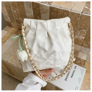 Detail of white quilted bucket bag with golden chain strap and tulip charm decoration