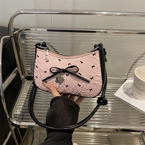 Pink crescent underarm bag with black bow print and metal heart pendant in a chic setup