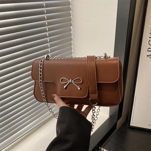 Sac bandoulière en cuir marron avec nœud argenté et chaîne sur un décor contemporain chic