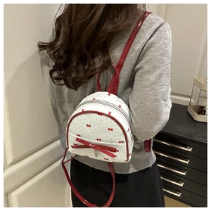 Detailed shot of a mini white backpack featuring red bow patterns and a large glossy bow