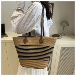 Detail of straw woven bucket bag featuring brown leather strap and contrast stitching