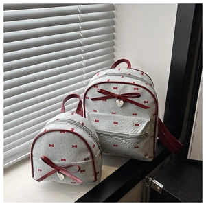 Detail of light gray canvas backpack set featuring red bow patterns and heart pendant
