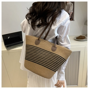 Detail of hand-woven straw tote with black stripes and brown leather shoulder straps