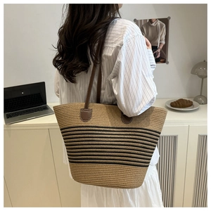 Detail of hand-woven straw tote bag with black stripes and brown leather handles