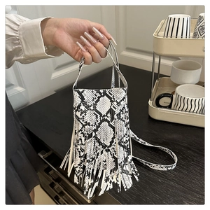 Detail of snake print texture and fringe tassels on small shoulder bag held by hand
