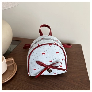 Close-up of mini backpack featuring red bow prints and a heart-shaped metal pendant