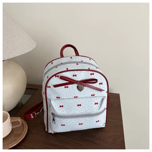 Close-up of small blue backpack with red bow patterns and heart-shaped metal pendant
