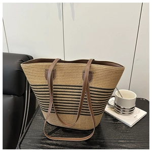 Detailed view of woven straw tote bag with black stripes and brown leather strap
