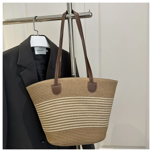 Detail of striped woven straw tote bag with brown leather handles on a blazer background