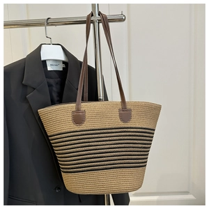 Close-up of handwoven straw tote with black stripes and brown leather straps on a hanger