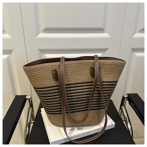 Detail of handwoven straw tote bag with striped pattern and dark brown leather handles