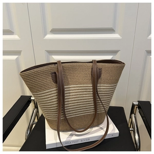 Detail of handwoven straw tote bag showing striped pattern and leather straps with stitching