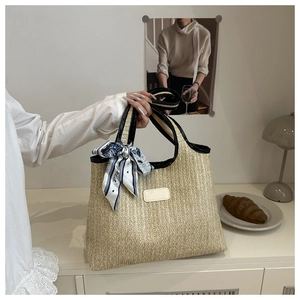 Close-up of woven straw tote bag with black leather trim and floral silk scarf detail