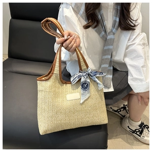 Detail of woven straw tote bag featuring brown leather trim and floral silk scarf