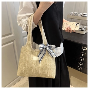 Detail of beige woven tote bag featuring a blue patterned silk scarf on the handle