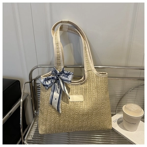Detail of woven straw tote bag featuring white leather handles and a blue printed silk scarf
