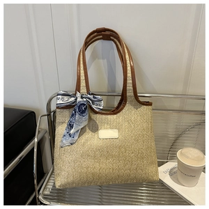 Detail of woven straw tote bag with brown leather handles and decorative Paris silk scarf