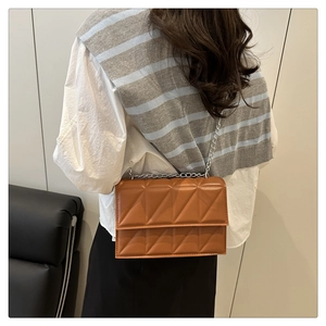 Detail of a brown quilted crossbody bag with silver chain strap on model shoulder