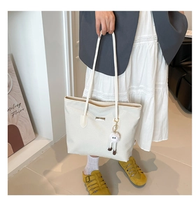 Gros plan du sac cabas blanc avec plaque en métal et breloque en peluche douce