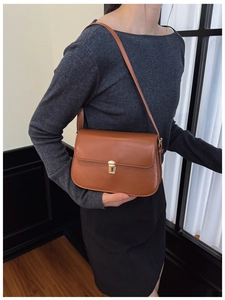 Close-up of brown leather shoulder bag with golden metal buckle and sleek flap design