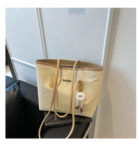 Détail du sac cabas en paille tissée avec anses en cuir et charm peluche sur canapé