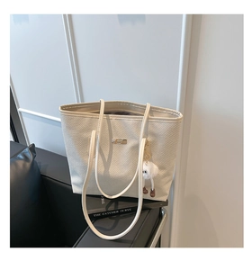 Détail d'un sac cabas tissé blanc cassé avec boucle dorée et pendentif en peluche