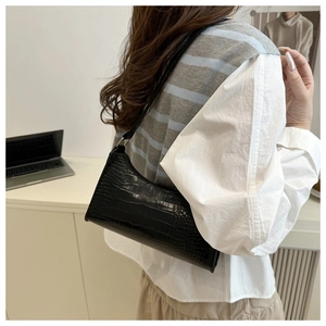 Model view of black croc-embossed baguette bag worn as a stylish underarm shoulder bag