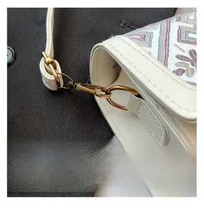 Detail of white PU leather bag with colorful floral embroidery and gold hardware