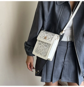 Detail of white mini crossbody bag with floral embroidery and golden metal buckle clasp