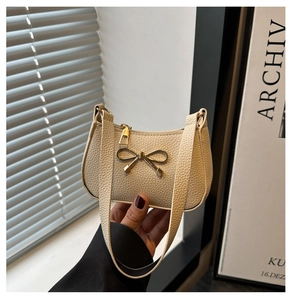 Detail of cream leather shoulder bag featuring a gold bow accent and pebble texture
