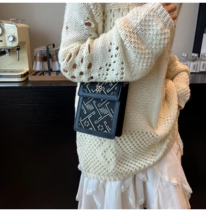 Detail view of black crossbody bag featuring a clover metal clasp and geometric texture