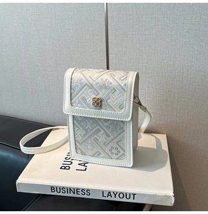Detailed embroidery on white bucket bag featuring a gold clover metal clasp and strap