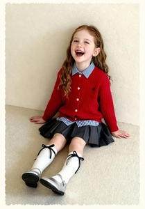 Detail of red cable knit cardigan with white buttons over a striped shirt for girls