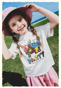 Niña con camiseta blanca de dibujos y pantalón rosa posando en la playa y césped
