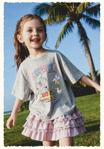 Niña con camiseta de dibujos y falda rosa de encaje corriendo en césped soleado