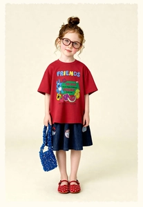 Plano detalle de camiseta roja de dibujos con falda bordada azul y accesorios infantiles