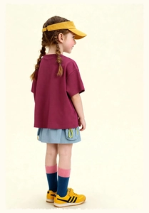 Niña con camiseta burdeos, falda azul, sombrero amarillo y zapatillas deportivas