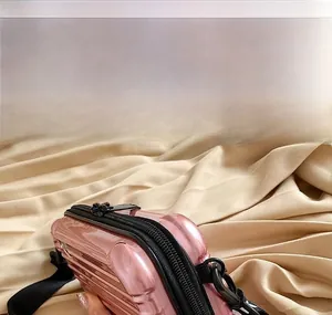Pink mini PC hard shell crossbody vanity bag with suitcase style ridges and black strap