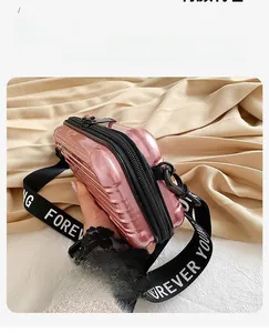 Pink mini suitcase bag with Forever Young strap held against beige background