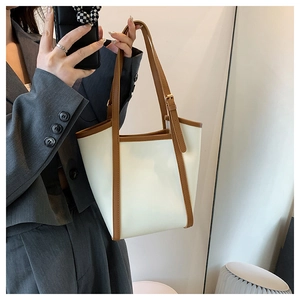 Detail of minimalist cream tote bag showing brown piping and gold adjustable buckle