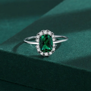 Macro detail of rectangle-cut emerald ring with white diamond halo on green velvet stand