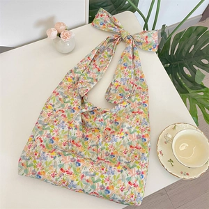 Detail view of floral print shoulder bag with decorative bow strap on a white surface