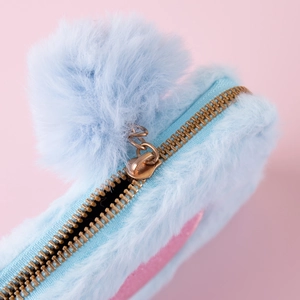 Detail of light blue plush pouch featuring a golden metal zipper and large soft pompom charm