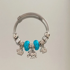Detail of silver cable charm bracelet featuring blue beads and three elephant pendants
