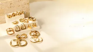 Détail de boucles d'oreilles créoles et clous géométriques en acier doré sur support blanc