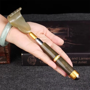 Detail of a deep green comb-shaped facial massage tool with a gold metallic handle